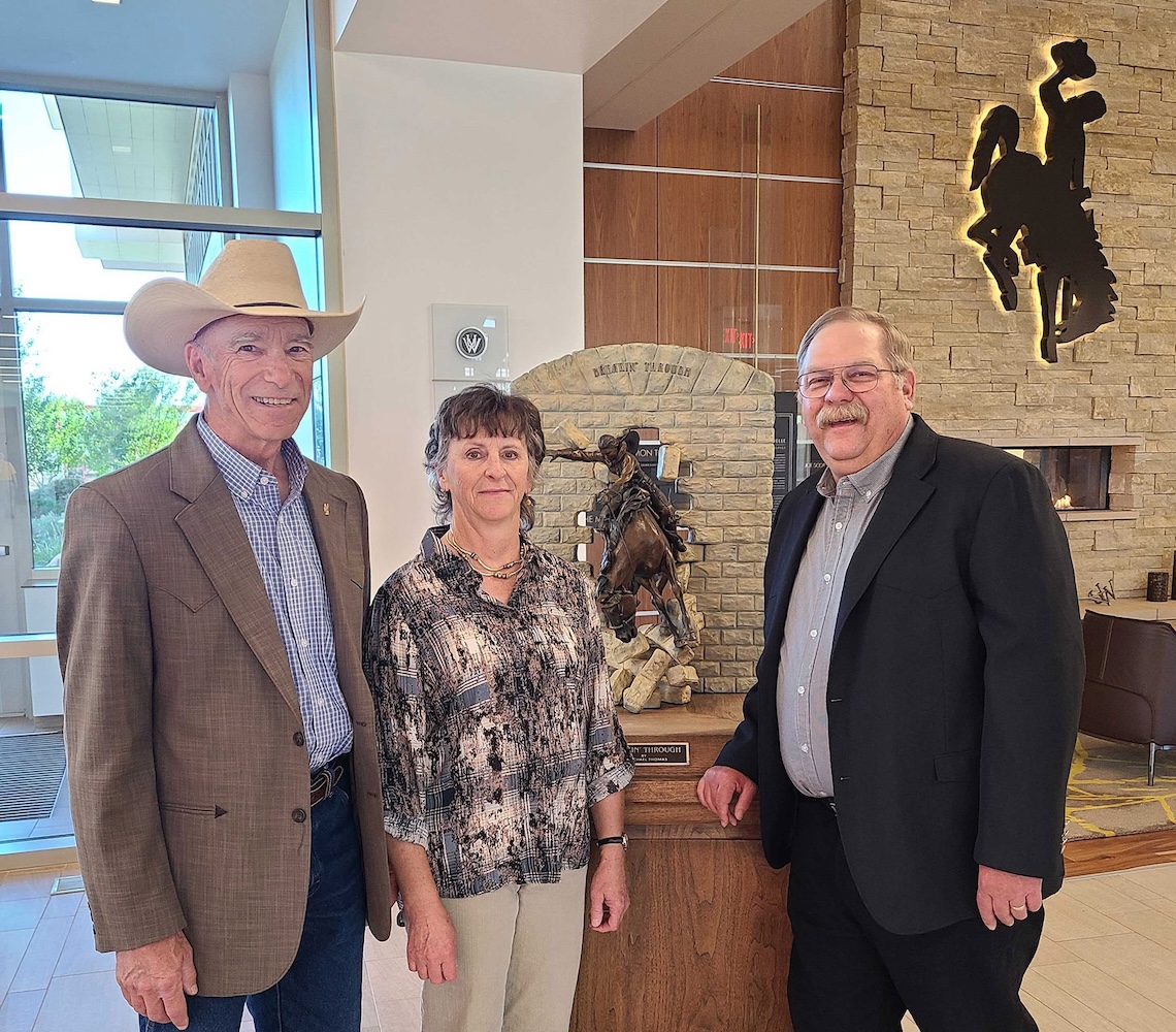 Doug Stark, Deniz Stark, and Chris Bastian stand in front of a statue of a horse rider breaking through a wall.