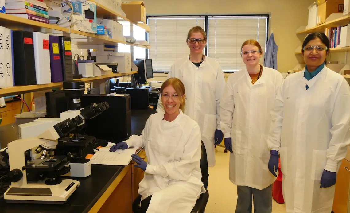 Mariela Srednik and lab workers wearing white lab coats and protective gloves in an office at the Wyoming State Vet Lab.