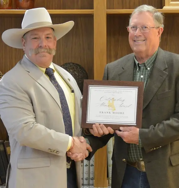 Frank Moore shakes hands with Kelly Crane and holds an award.