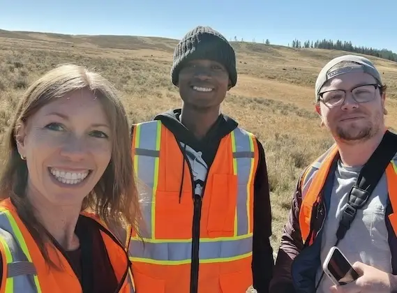 Mariela Srednik and two students, all wearing orange reflective vests, pose for a selfie at a Yellowstone research site