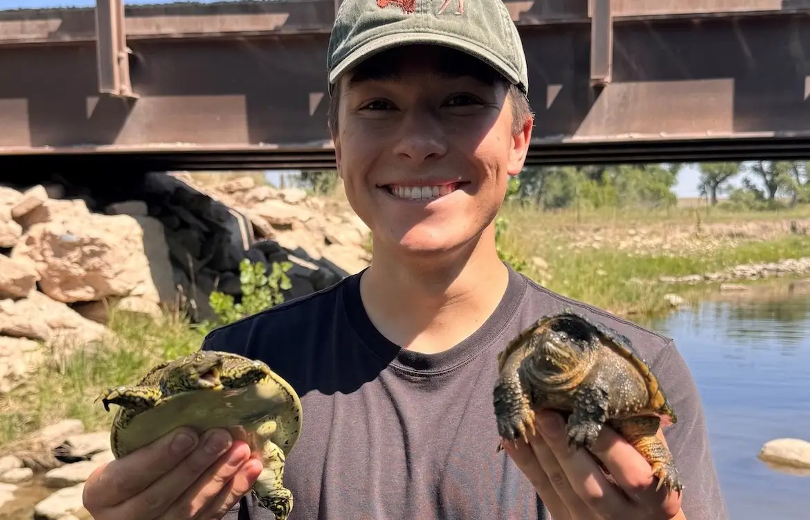 Camden Foley holds a turtle in each hand by a river.
