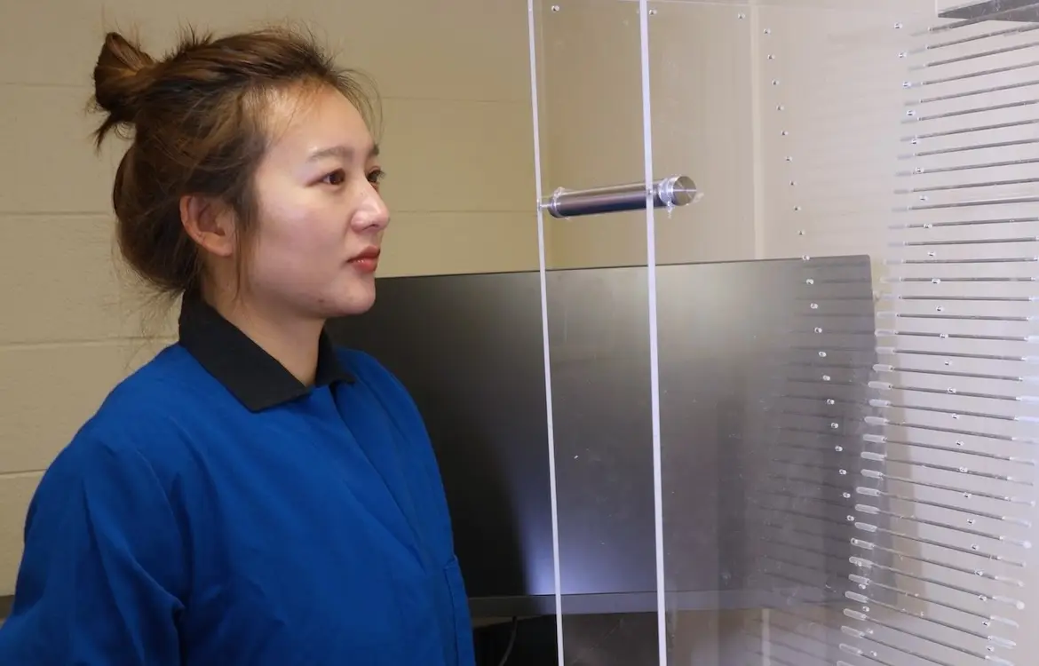 Mingming Yang stands in front of a monitor and a steep plastic ladder.